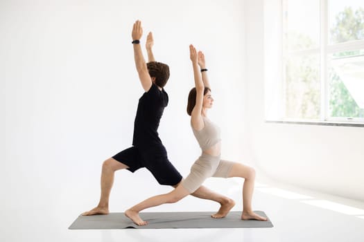 Cheerful young european guy and woman in sportswear do hand exercises, practice yoga on mat