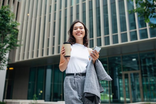 Young Businesswoman With Smartphone Holding Coffee Posing In Urban Area