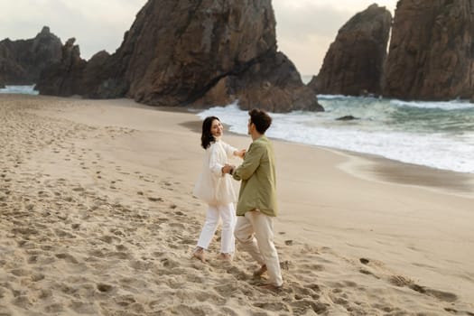 Full length shot of loving young couple having fun on the beach, holding hands and enjoying date on the ocean shore