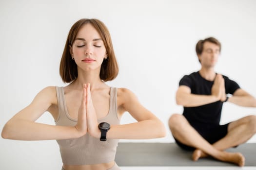 Calm young european guy and woman in sportswear with closed eyes do meditate, practice yoga