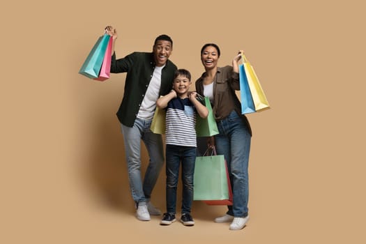 Thrilled international family enjoying shopping together, isolated on beige