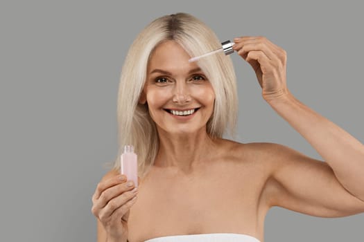Anti-Age Cosmetics. Attractive Mature Woman Applying Face Serum With Droplet On Face