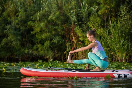 Young woman are doing yoga on a stand up paddle board SUP on a beautiful lake or river