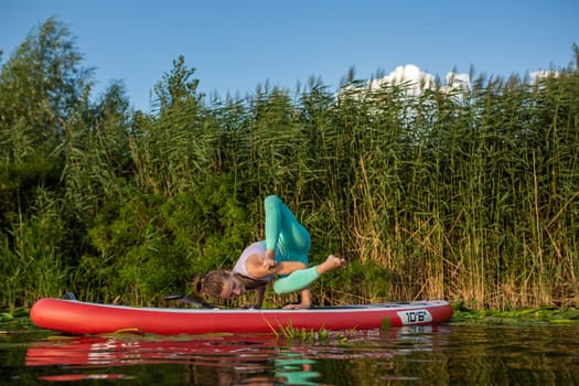 Photo of young woman doing hand stand on stand up paddle board. She wearing a leggings and top.