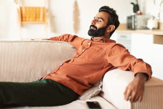 Indian guy lying on comfortable couch resting at home
