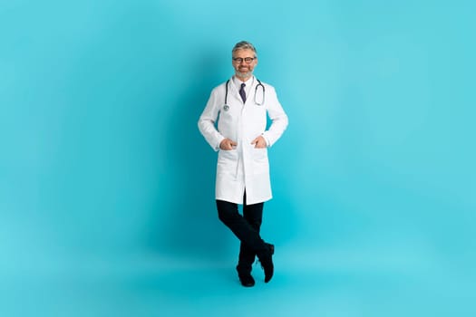 Positive friendly mature doctor posing on blue background