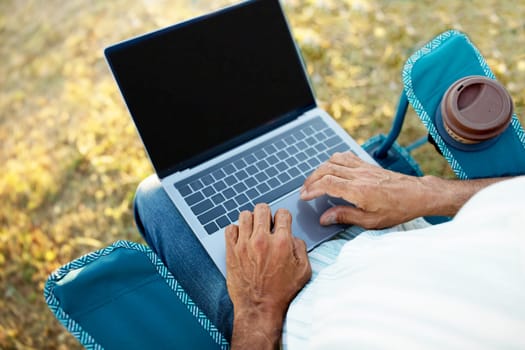 Senior Man Holding Computer Sitting In Touristic Chair Outdoor, Closeup