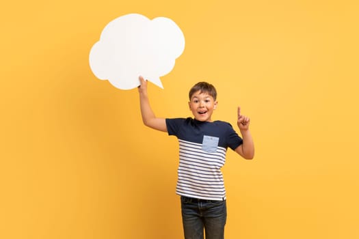 Smiling casual boy holding white paper communication bubble, pointing up
