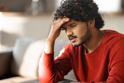 Portrait Of Depressed Young Indian Man Sitting On Couch At Home