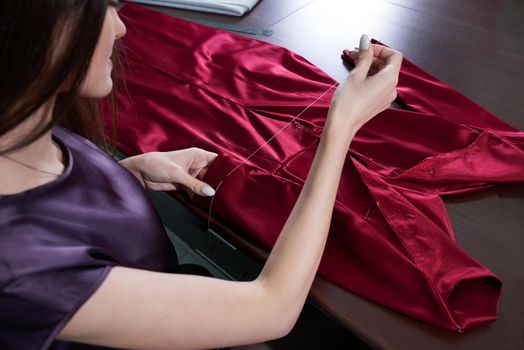 Beautiful young dressmaker in workroom sewing red dress in tailor studio or atelier shop