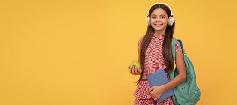 smiling school child in headphones carry backpack and workbook with apple for lunch. Portrait of schoolgirl student, studio banner header. School child face, copyspace.