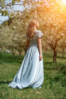 Blond garden. Portrait of a blonde in the park. Happy woman with long blond hair in a blue dress.