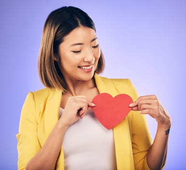 Asian girl, support and paper heart for care with smile in studio with purple background with asian. Peace, wellness and woman with love sign for kindness or hope with happiness and romance emoji