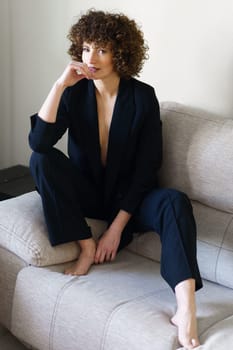 Woman in suit with bare chest sitting on sofa