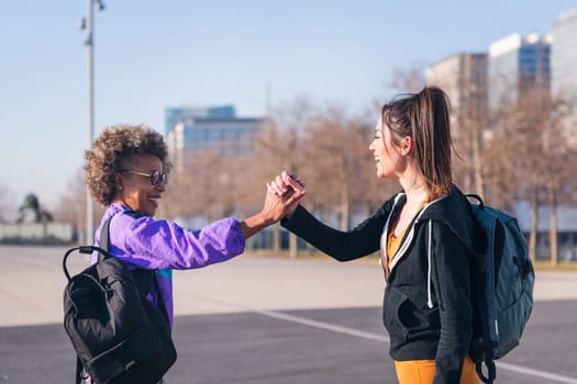 portrait of two happy sportswomen shaking hands before running in the city, concept of friendship and sportive lifestyle