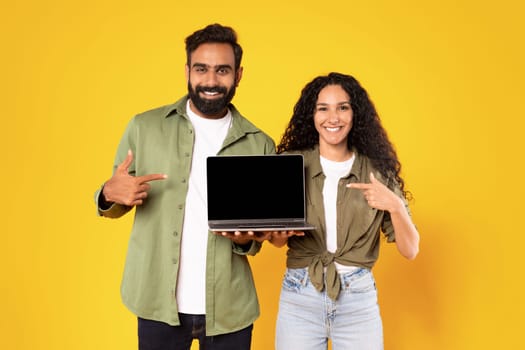 Arabic Couple Holding Laptop Pointing At Computer Screen In Studio