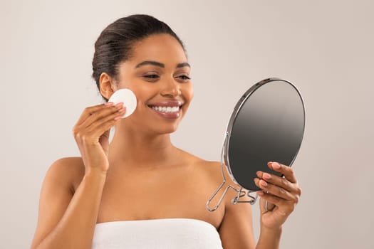 Happy attractive african american woman applying face toner and smiling