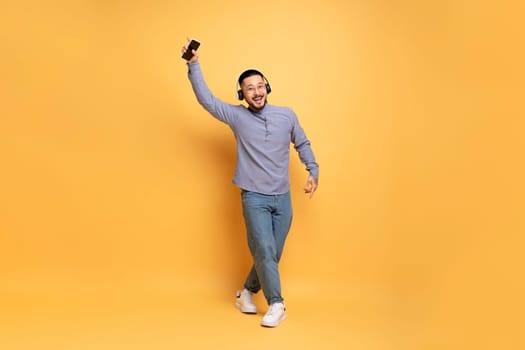 Cheerful asian man in wireless headphones listening music on smartphone and dancing