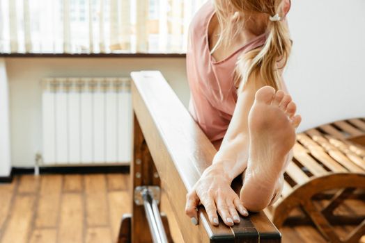 Middle aged woman stretching legs on wooden beam in gym before yoga excercise