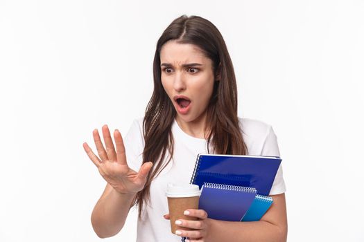 Education, university and studying concept. Close-up portrait of shocked young woman holding notebooks and learning material staring at her hand with shock as she broke her finger, need go salon