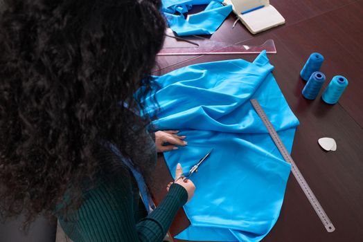 Dressmaker cutting blue fabric in tailor studio, atelier shop