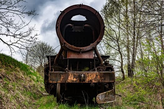 Rusted steam locomotive with coal car abandoned at train cemetery on old rail track.
