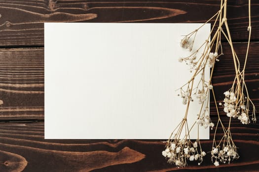 Blank sheet of paper with flower branch on wooden background