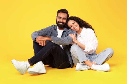 Happy Arab Family Couple Sitting And Embracing Over Yellow Background