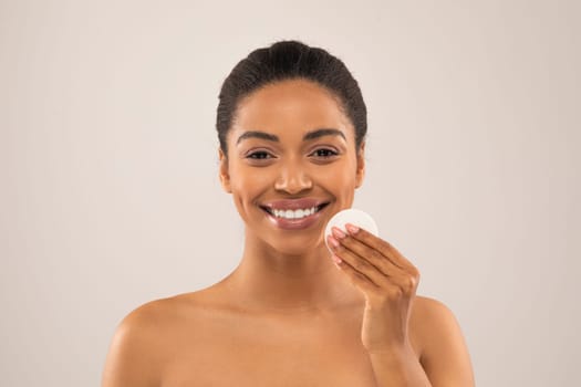 Closeup of smiling pretty young black woman using cotton pad