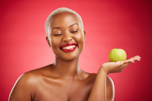 Happy black woman, apple and natural nutrition for healthy diet against a red studio background. African female person smile with natural organic green fruit for food snack, health and wellness