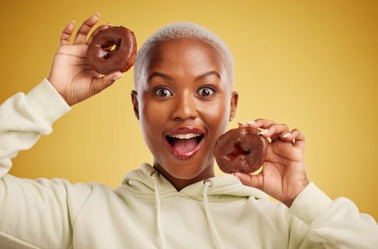 Portrait, chocolate and donut with a black woman in studio on a gold background for candy or unhealthy eating. Smile, food and baking with a happy young female person holding sweet pastry for dessert