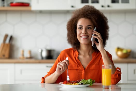 Smiling Black Woman Talking On Cellphone And Enjoying Tasty Breakfast In Kitchen