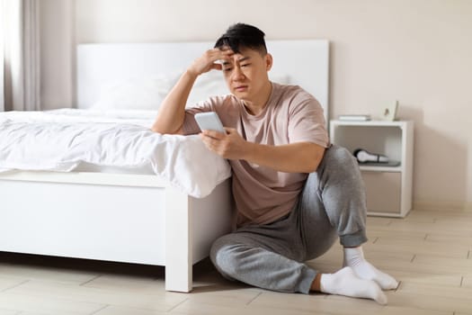 Unhappy depressed chinese businessman using phone in bedroom