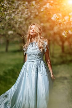 Blond blooming garden. Portrait of a blonde in the park. Happy woman with long blond hair in a blue dress.