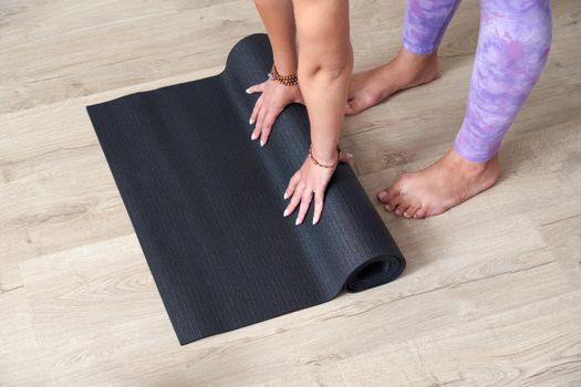 woman frolling black yoga or fitness mat after working out at home in living room. Healthy life, yoga concepts