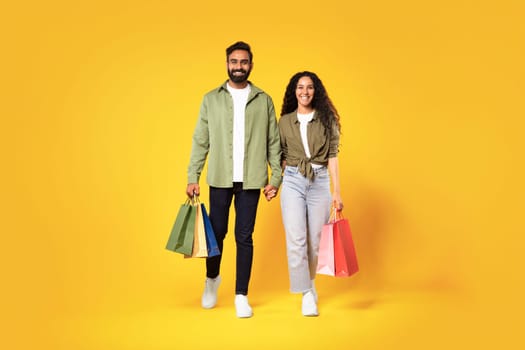 Arabic man and woman holding shopping bags walking, yellow background