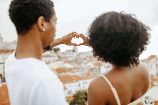 Glad millennial african american man hugging woman, making heart sign with hands in city, enjoy walk