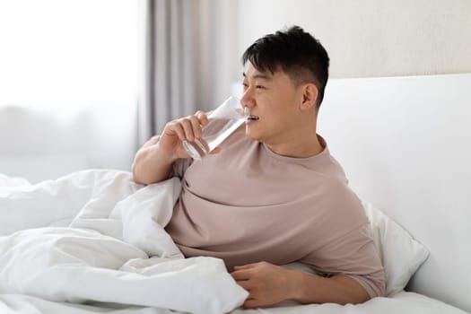 Middle aged asian man drinking water after waking up