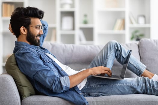 Networking Concept. Indian Guy In Casual Clothes Using Laptop In Living Room
