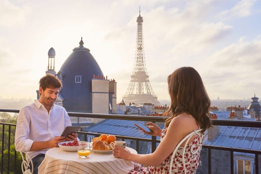 Travel, breakfast and couple in Paris with the Eiffel Tower on a terrace for romance or anniversary. City, vacation or tourism tech app with a man and woman eating food while looking at a view.