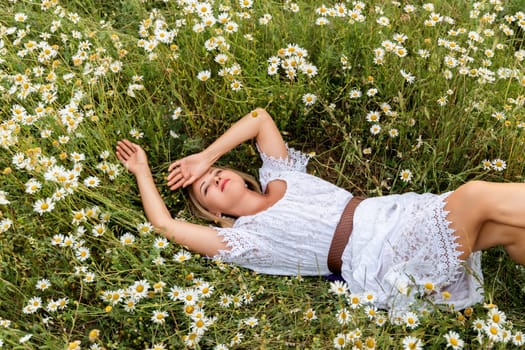 A woman lies in a chamomile field, dressed in a white dress