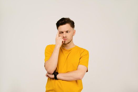 Lost in thought or deep in thought handsome young man folded his hands and holding his face with his hand. Young casual man in yellow t-shirt portrait isolated on white background
