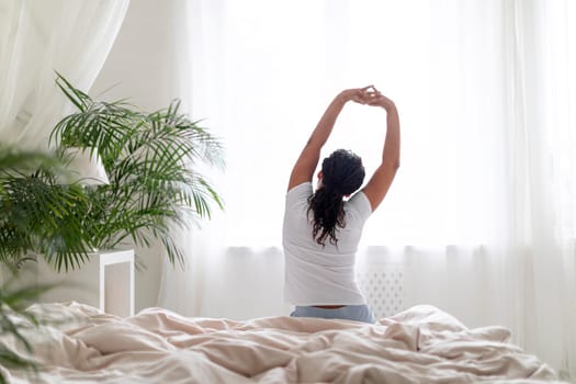 Young Black Woman Sitting In Bed And Stretching Arms After Waking Up
