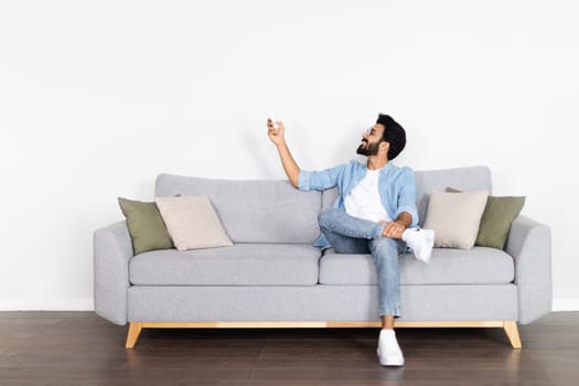 Relaxed middle eastern guy chilling on couch, turning on AC
