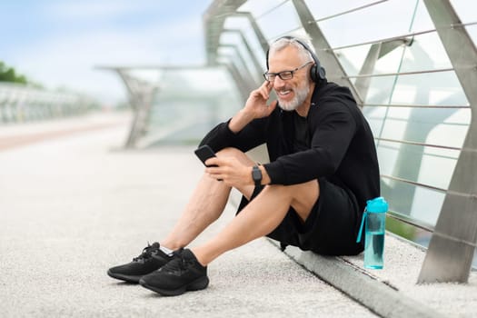 Elderly sportsman having break while jogging outdoor, listening to music