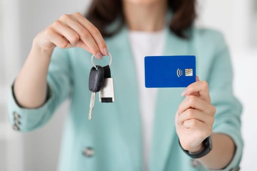 Young european lady manager in suit shows keys and credit card in office, close up, cropped