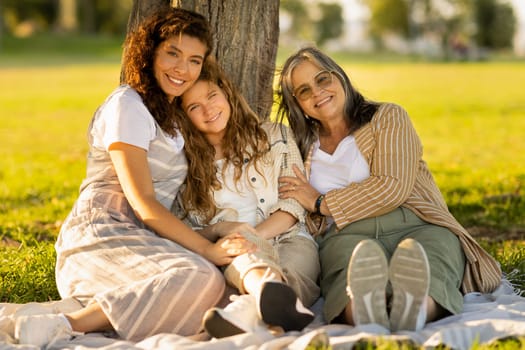 Smiling pretty european multi-generation women enjoy picnic on paid in park, outdoor