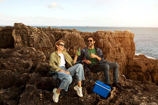 Happy Young Man And Woman Relaxing On Rocks Near Ocean Shore