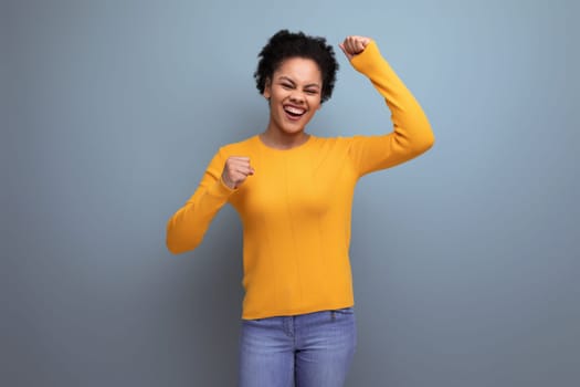 pretty confident 20s latin woman with afro hair in casual yellow sweater on studio background with copy space