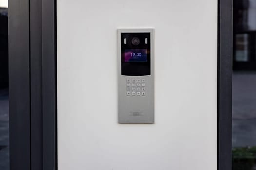 Doorbell with video camera and microphone, on the white wall of an apartment building, doorbell camera